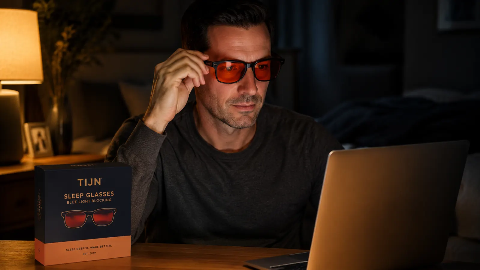 Close-up of hands putting on TIJN blue light blocking glasses in front of a laptop at night